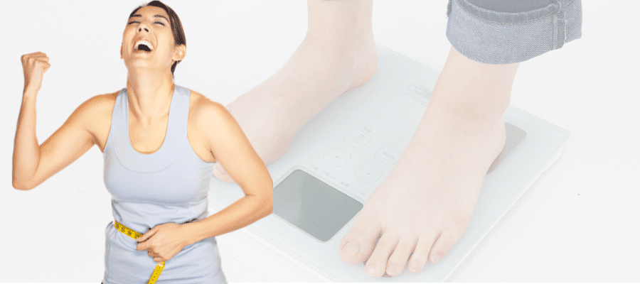 Happy woman in gray sports bra celebrating with fist pump while measuring waist with yellow tape measure